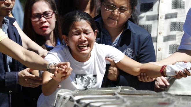 A distraught woman, held by those around her, grieves in front of a long wooden box carrying her sister's remainsImage copyrightEPA Image caption Ms Demafelis's sister cried over her casket upon its arrival in Manila last week