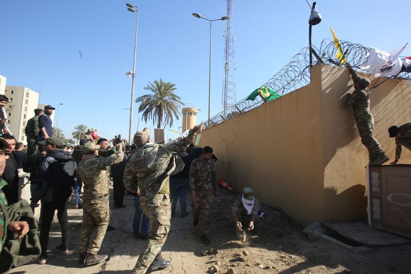 Members of Iraq's pro-Iranian Hashd al-Shaabi paramilitary group hang flags on the barbed wire of the outer wall of the US embassy in Baghdad during an angry demonstration on December 31, 2019 to denounce weekend US air strikes that killed Iran-backe