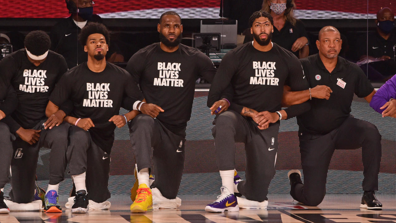 Quinn Cook #28, LeBron James #23 and Anthony Davis #3 of the Los Angeles Lakers kneel for the National Anthem with Doc Rivers of the LA Clippers on July 30, 2020 in Orlando, Florida at The Arena at ESPN Wide World of Sports. © David Dow, AFP