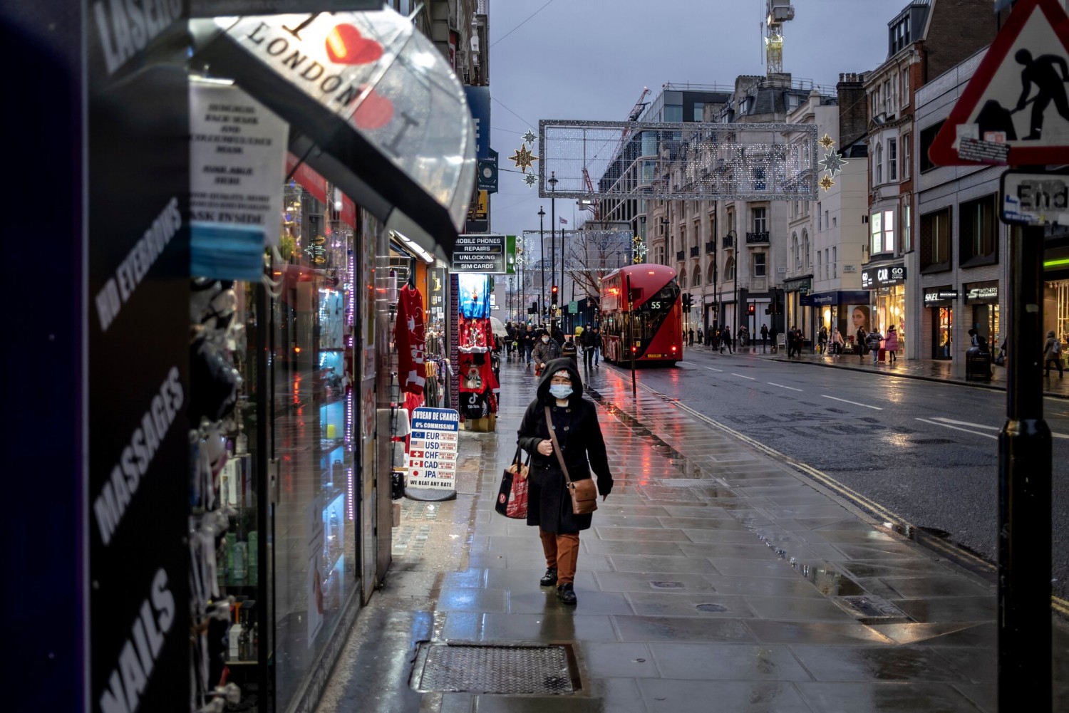 A woman walks on a rain-soaked Oxford Street on the first day of Tier 3 restrictions in London. The city has been moved to even tighter restrictions.Credit...Andrew Testa for The New York Times
