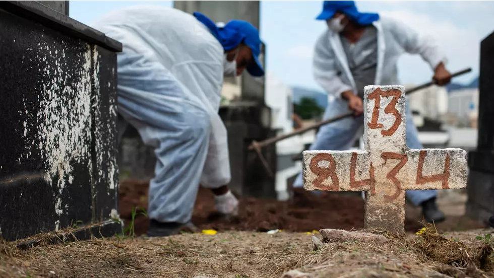 Cemetery workers, wearing protective gear, shovel dirt onto the coffin containing the remains of a Covid-19 victim at the Inahuma cemetery in Rio de Janeiro, Brazil, Wednesday, April 28, 2021. © Bruna Prado, AP