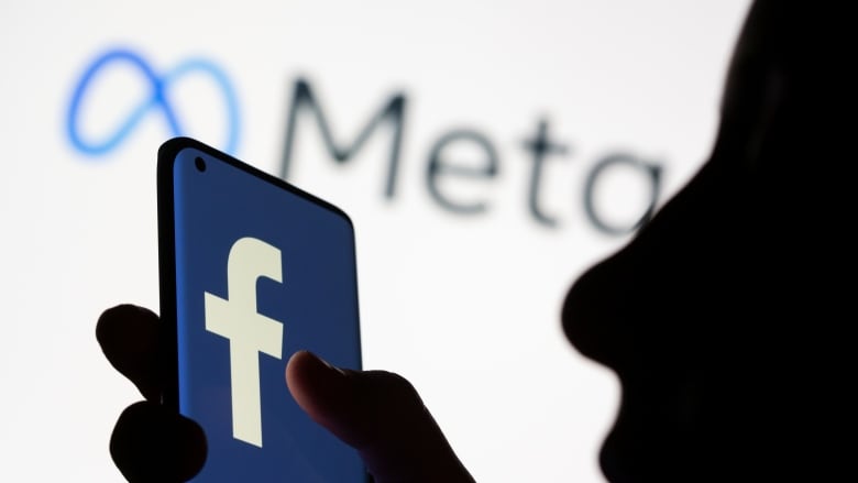 A woman holds smartphone with the Facebook logo in front of a the logo of its parent company, Meta. The company is ending news availability on its platforms in Canada. (Dado Ruvic/Reuters)