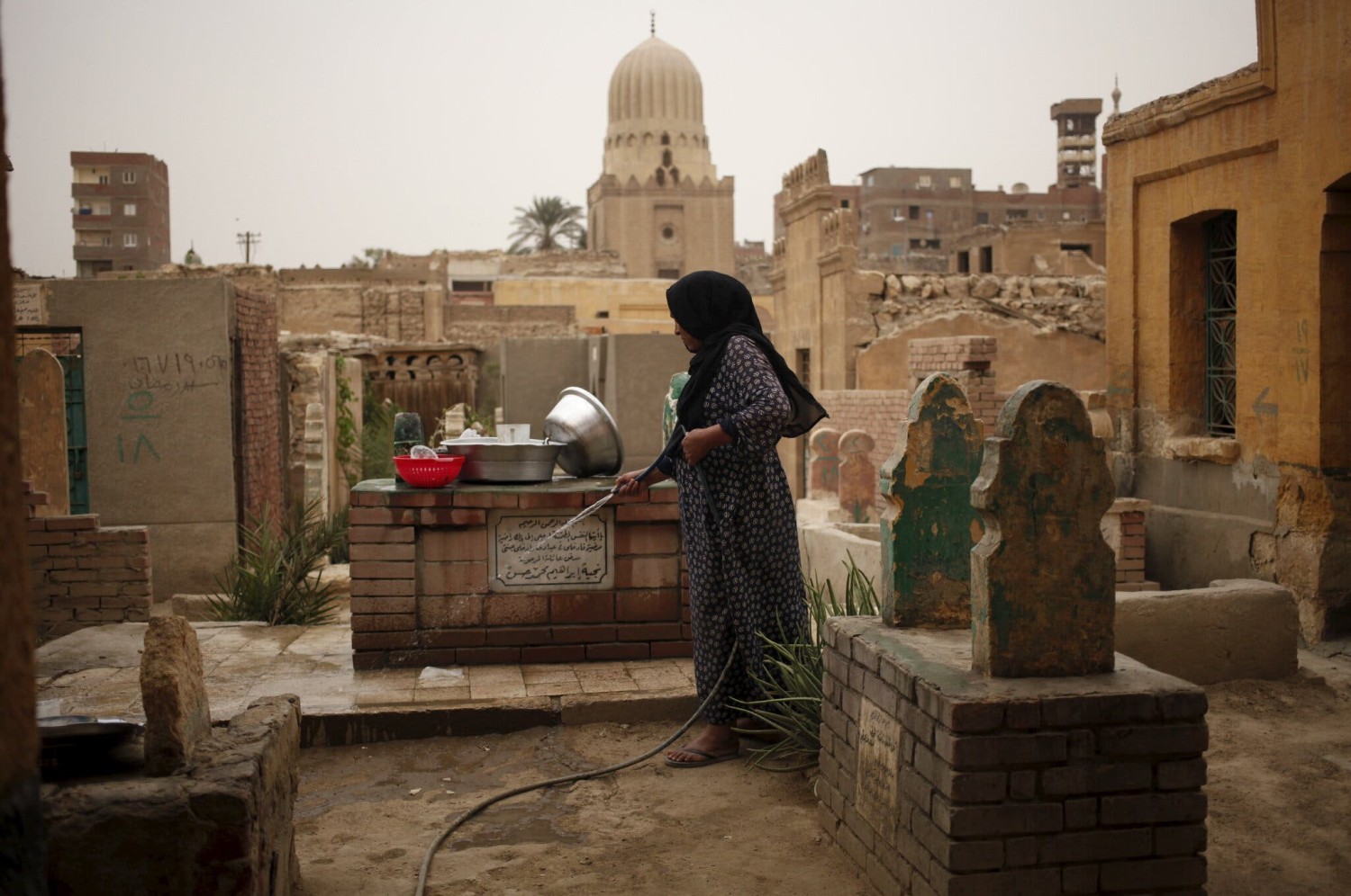 A woman cleans tombs in Cairo’s City of the Dead cemetery.Credit...Asmaa Waguih/Reuters