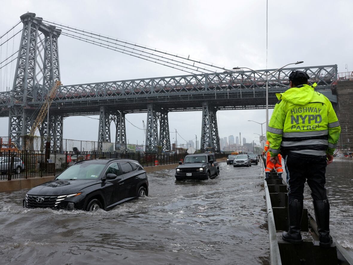 police officer looks on as motorists drive through a flooded street in New York City on Friday. New York and its surrounding areas were swamped by a potent rainstorm. (Andrew Kelly/Reuters)