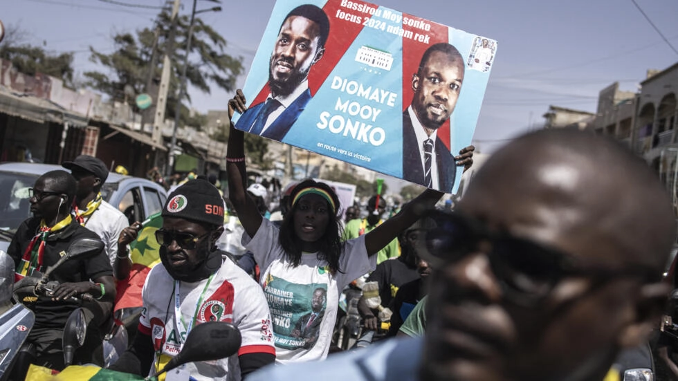 A supporter holds up a poster showing presidential candidate Bassirou Diomaye Faye and opposition leader Ousmane Sonko during a campaign march on March 10, 2024. © John Wessels, AFP
