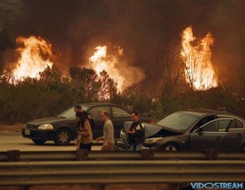 A woman involved in a traffic accident waits to get towed beside a wall of flames on the 101 highway during the Thomas wildfire near Ventura, Calif. on Dec. 6, 2017.