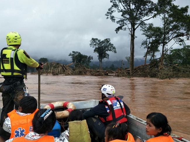 This handout photo from the Thai Rescue Team shows a member of the team riding in a raft with rescued flood survivors close to the swollen river in Attapeu province. Picture: AFPSource:AFP
