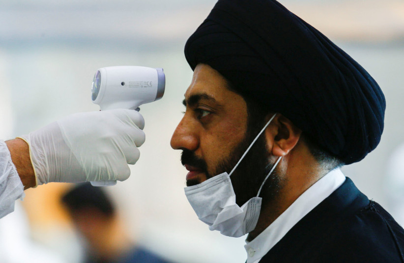 A medical staff member in protective gear checks the temperature of a cleric man amid concerns over the coronavirus (COVID-19) spread, at Najaf airport in the holy city of Najaf upon his arrival from Iran, Iraq March 15, 2020. (photo credit&#x