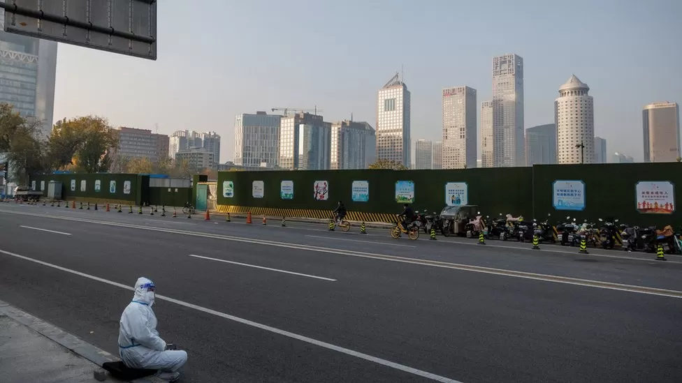 REUTERS/An epidemic prevention worker in a protective suit sits on the pavement in Beijing's Central Business District