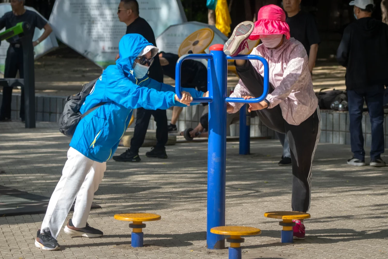 Women wearing face masks use exercise equipment at a public park in Beijing in May 2023. Mark Schiefelbein—AP Photo