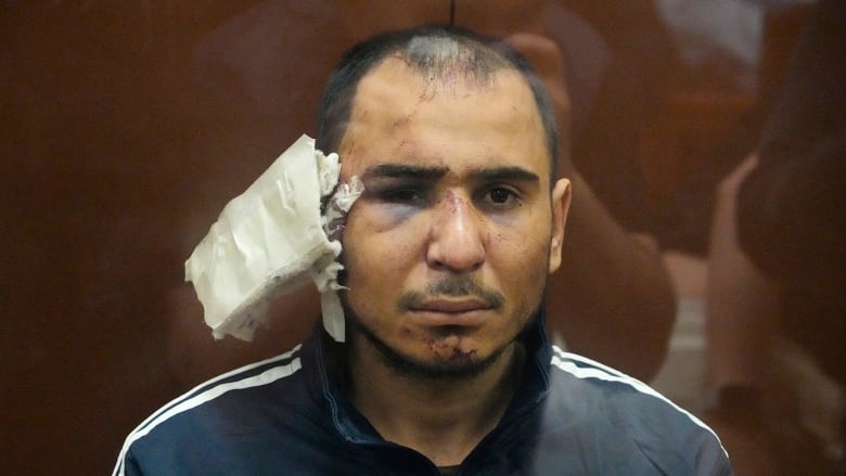 Saidakrami Rachabalizoda, a suspect in Friday's deadly Crocus City Hall shooting, sits in a glass cage in a Moscow courtroom on Sunday with a heavily bandaged ear. (Alexander Zemlianichenko/The Associated Press)