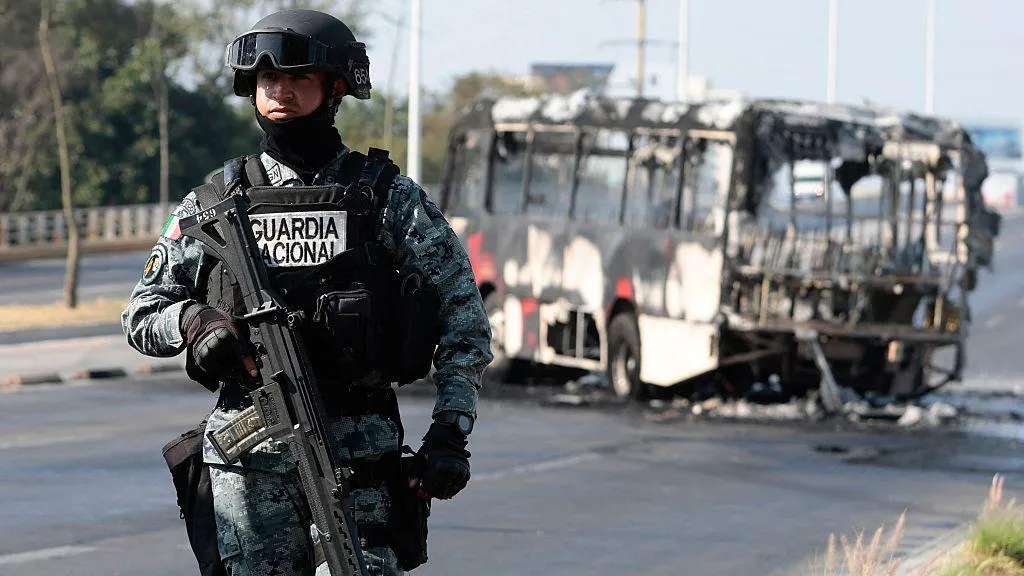 Getty Images / A member of Mexico's National Guard stands near the charred wreckage of bus that appears to have been set on fire by organised crime groups in Jalisco state on Sunday