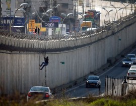 A Palestinian man uses a rope to climb over a section of Israel's controversial separation barrier that separates the West Bank city of al-Ram from east Jerusalem on Feb. 24, 2016. Many Palestinians from the West Bank cross illegally into Israel